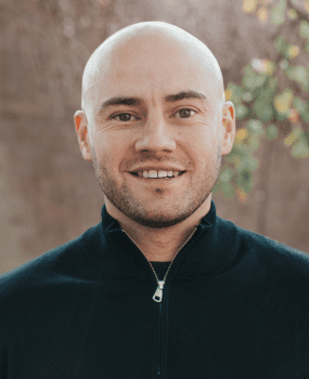A smiling bald man dressed in a black jacket poses for the photo.